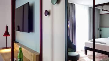 Une chambre d’hôtel avec un lit, un téléviseur fixé au mur, une table de chevet avec une bouteille et des verres, et une chaise.