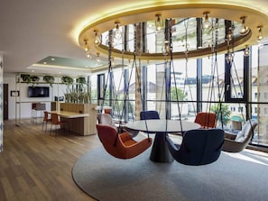 A modern interior with a central round table, hanging chairs, a TV, and large windows.