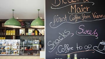 A cafe interior with a chalkboard menu, hanging green pendant lights, and a display case with snacks and beverages.