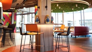 A modern interior with a central wooden reception desk, black and orange chairs, and a red sofa. - ibis Styles Parndorf Neusiedler See (Parndorf)