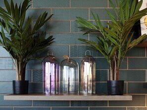 A shelf with three glass jars and two potted plants against a tiled wall. - ibis Styles Parndorf Neusiedler See (Parndorf)