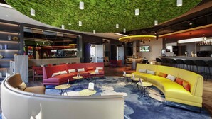 A modern hotel lobby with a green textured ceiling, a bar area, and seating arrangements including sofas and chairs. - ibis Styles Parndorf Neusiedler See (Parndorf)