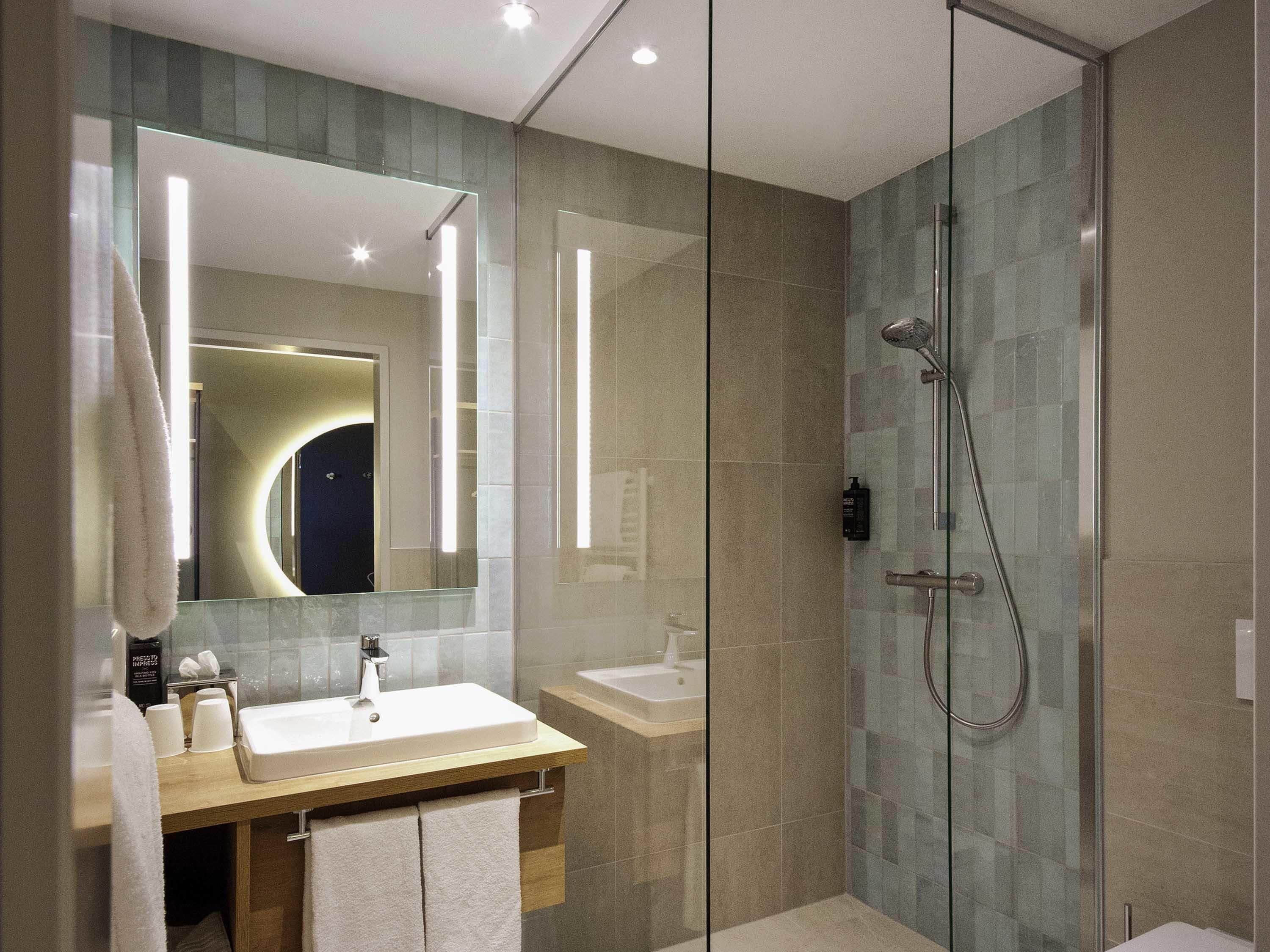A modern bathroom with a glass-enclosed shower, a vanity with a sink, and a large mirror.