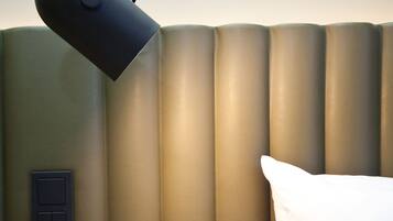 Et moderne hotelværelse med en stor seng, en sort skrivebordslampe og en stikkontakt på væggen.