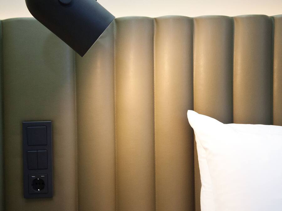 Et moderne hotelværelse med en stor seng, en sort skrivebordslampe og en stikkontakt på væggen.