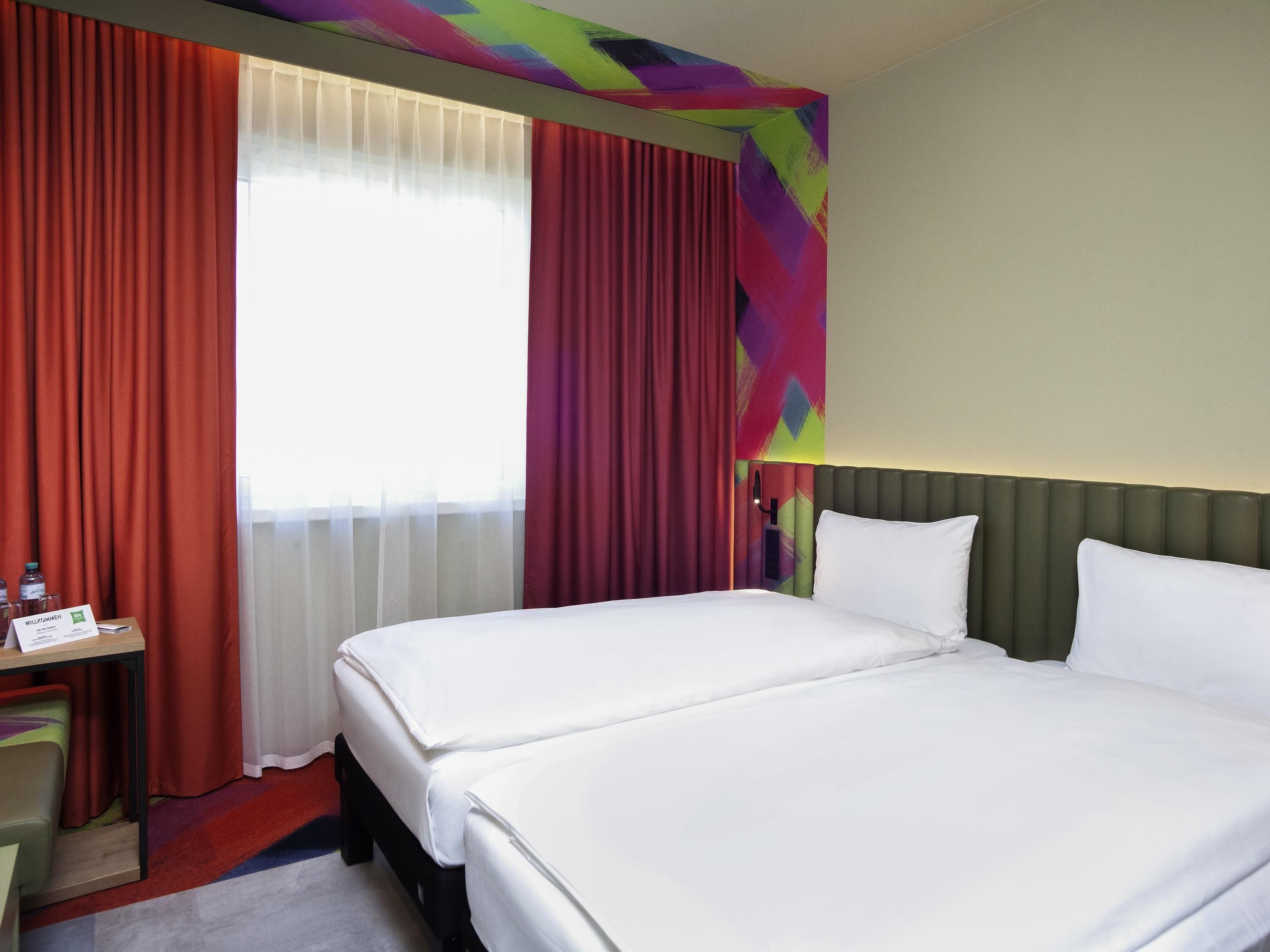 Ett hotellrum med två sängar, ett skrivbord med en stol och ett fönster med gardiner.