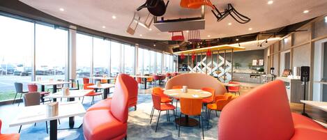 Un restaurante moderno con asientos naranja, ventanas amplias y vista al estacionamiento.