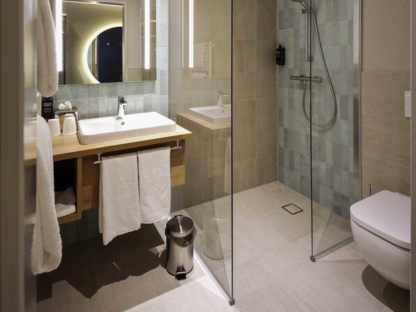 A modern bathroom with a glass-enclosed shower, a sink, and a toilet. - ibis Styles Parndorf Neusiedler See (Parndorf)