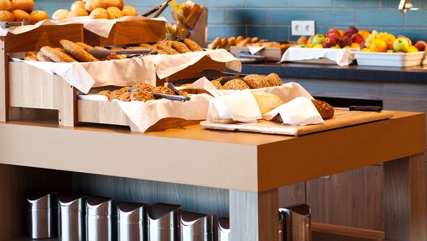 A breakfast buffet with various pastries and fruits, a wooden counter, and hanging pendant lights. - ibis Styles Parndorf Neusiedler See (Parndorf)