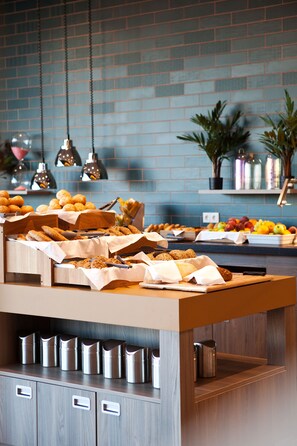 A breakfast buffet with various pastries and fruits, a wooden counter, and hanging pendant lights. - ibis Styles Parndorf Neusiedler See (Parndorf)