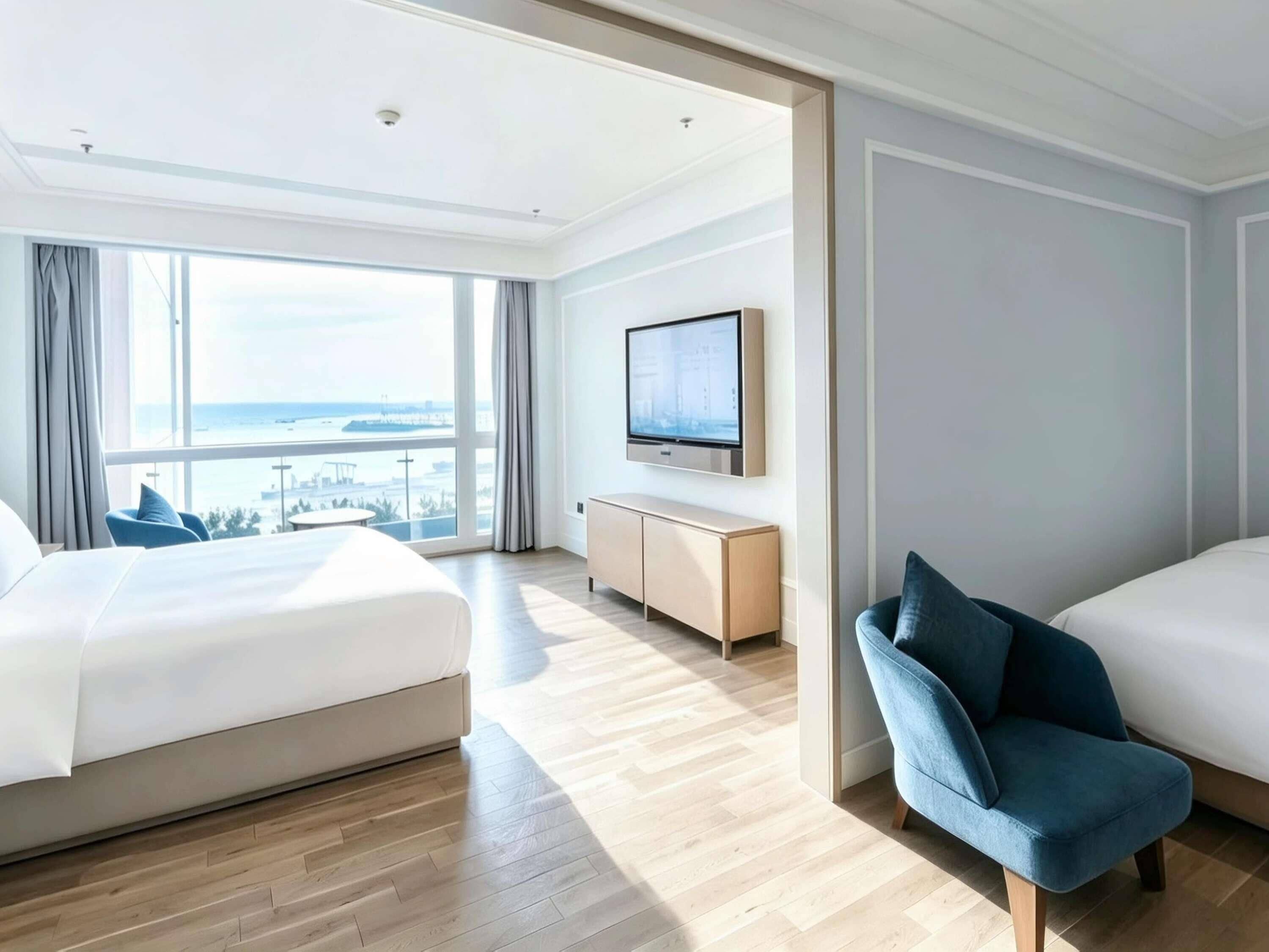 A hotel room with a large bed, a smaller bed, a TV mounted on the wall, and a view of the sea.