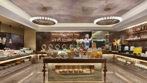 Un hall d’hôtel avec un sol en marbre, une table de buffet centrale et une statue représentant un chef cuisinier.