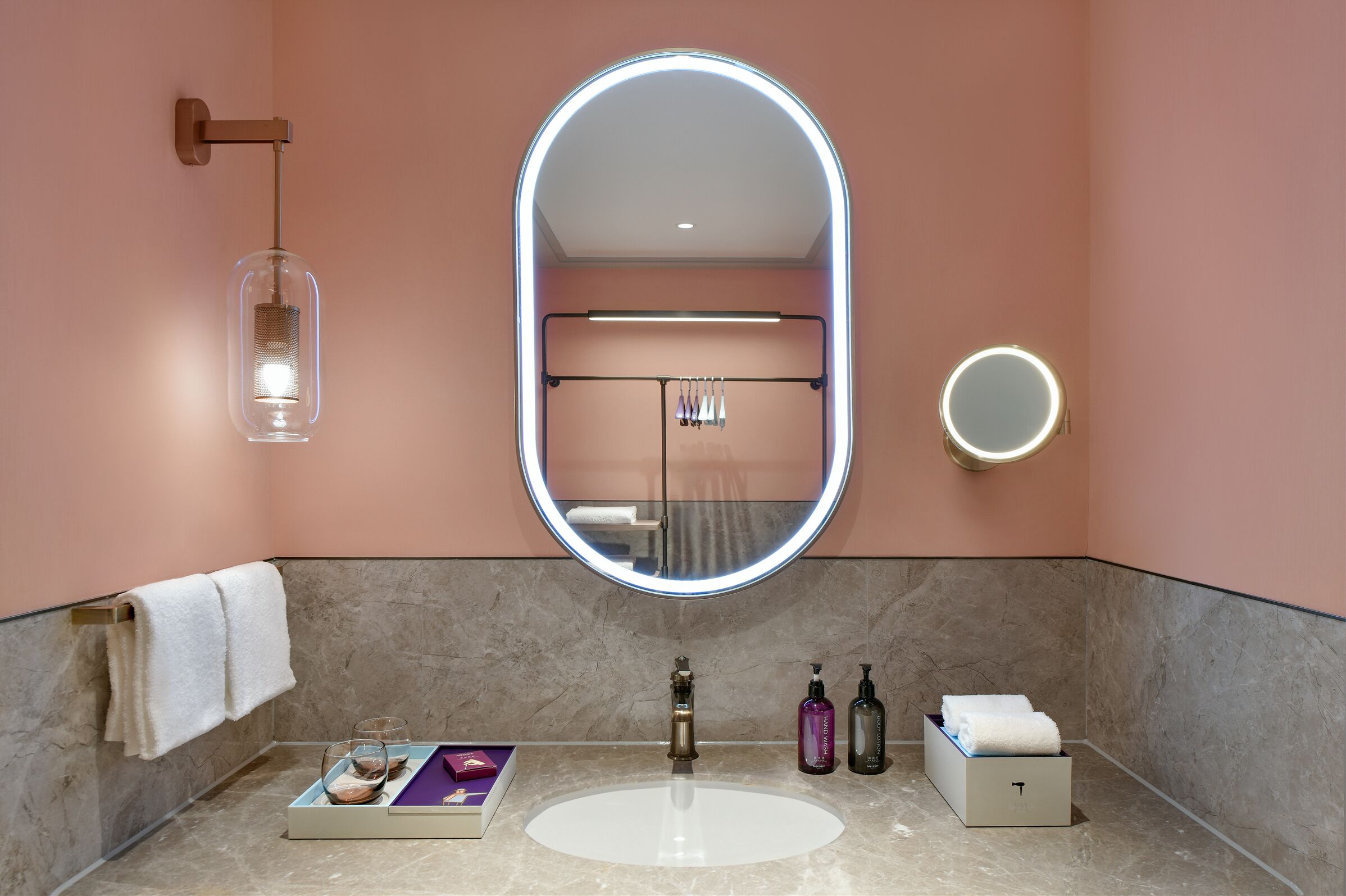 A bathroom with a large oval mirror, a towel rack, a glass bottle, and a soap dispenser.