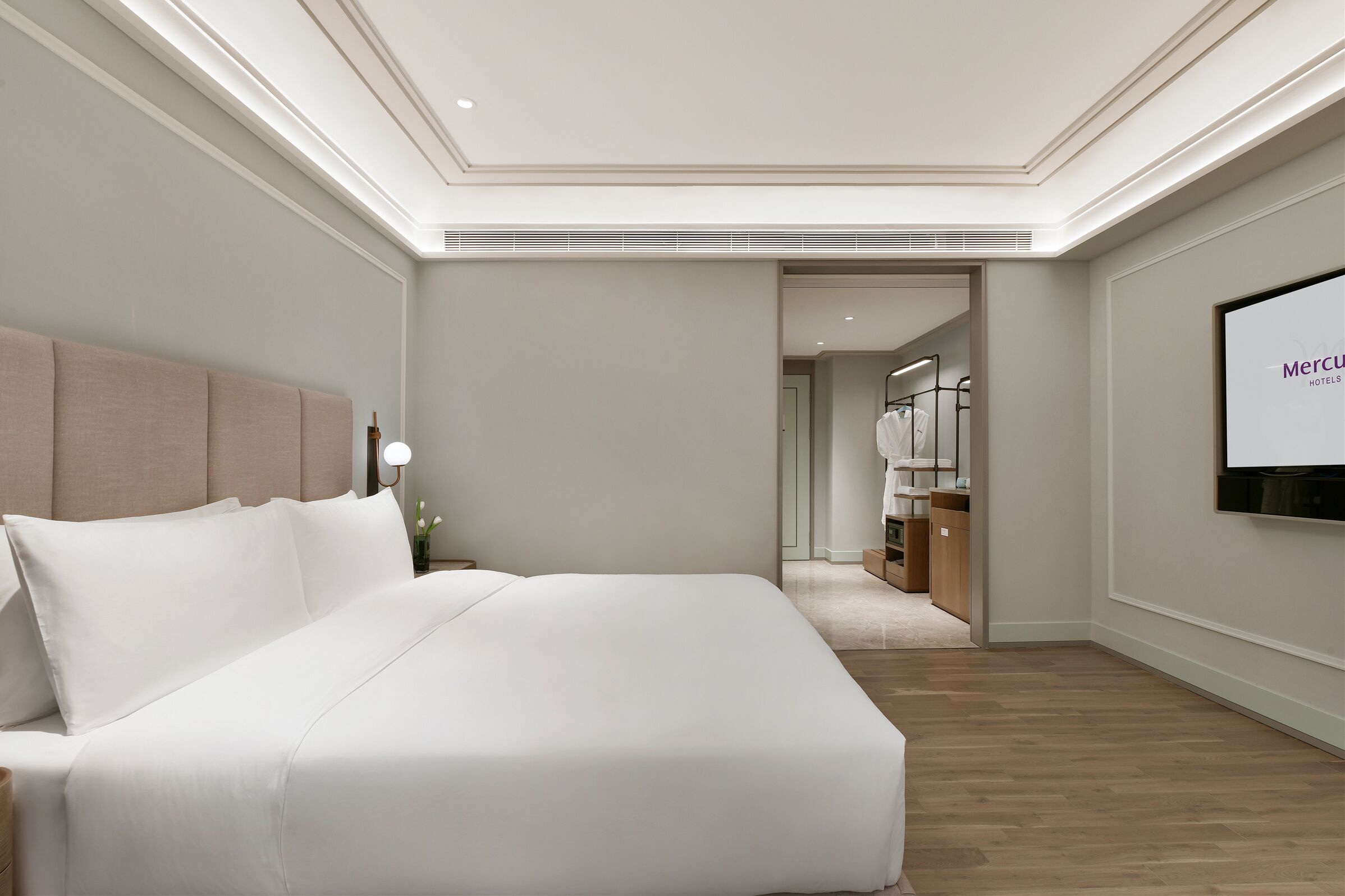 Habitación de hotel con una cama grande, un televisor instalado en la pared y un pasillo que conduce a un baño.