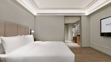 Habitación de hotel con una cama grande, un televisor instalado en la pared y un pasillo que conduce a un baño.