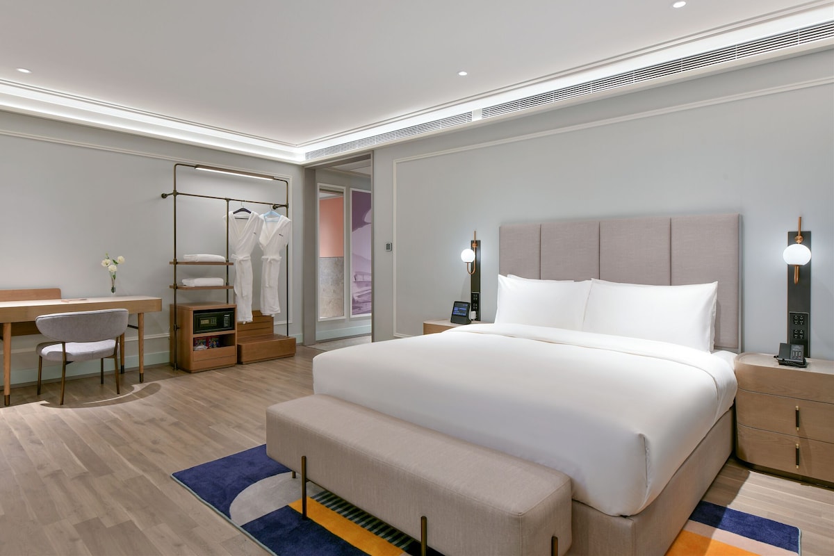 A modern hotel room with a large bed, bedside tables, a desk, and a chair.