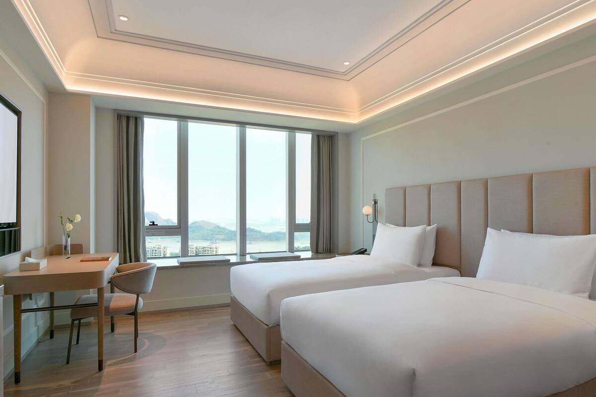 Quarto de hotel com duas camas, uma escrivaninha e uma cadeira.