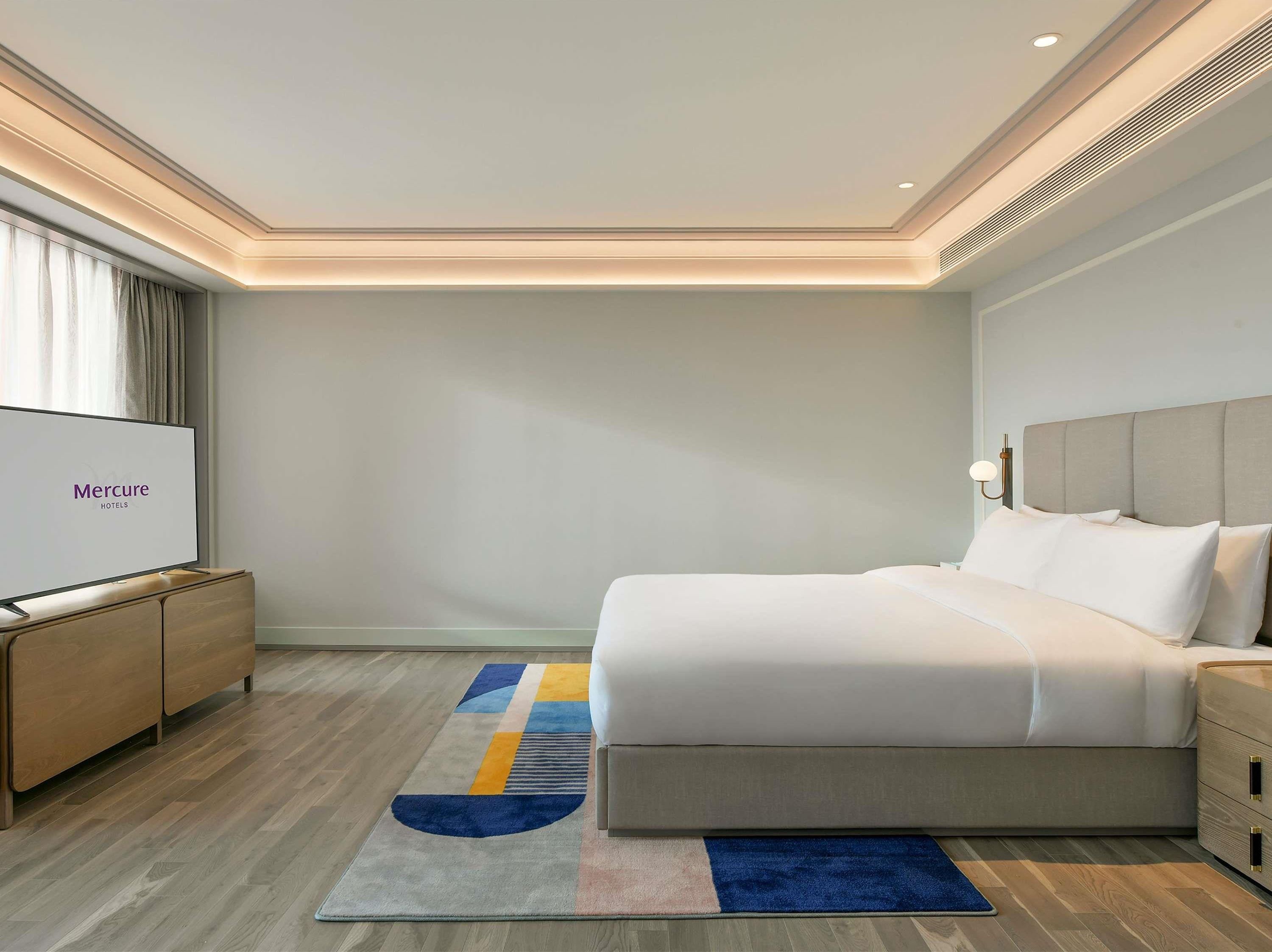 Een moderne hotelkamer met een groot bed, een flatscreen televisie, een houten nachtkastje en een decoratief vloerkleed.
