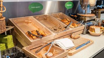 Un bufé con diferentes alimentos en recipientes transparentes, incluyendo bollería y pan.