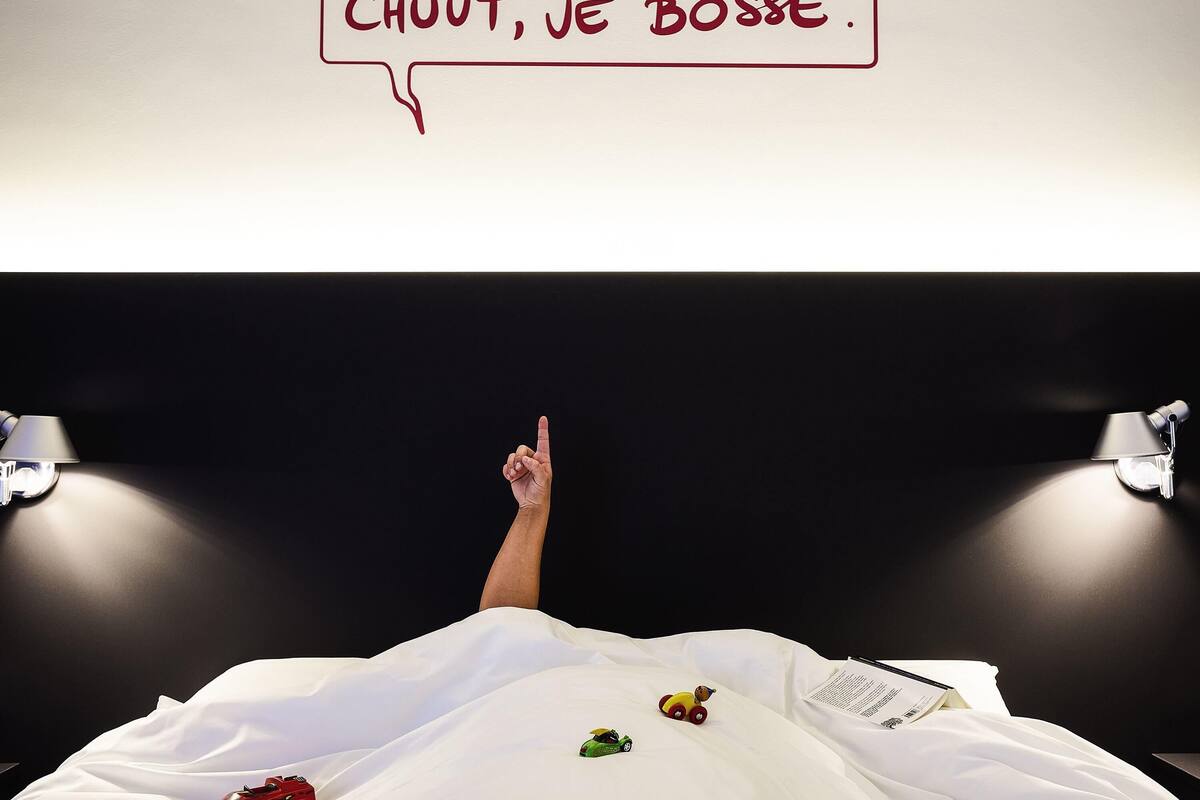 A bed with a white comforter, a toy car, and a toy truck on it.
