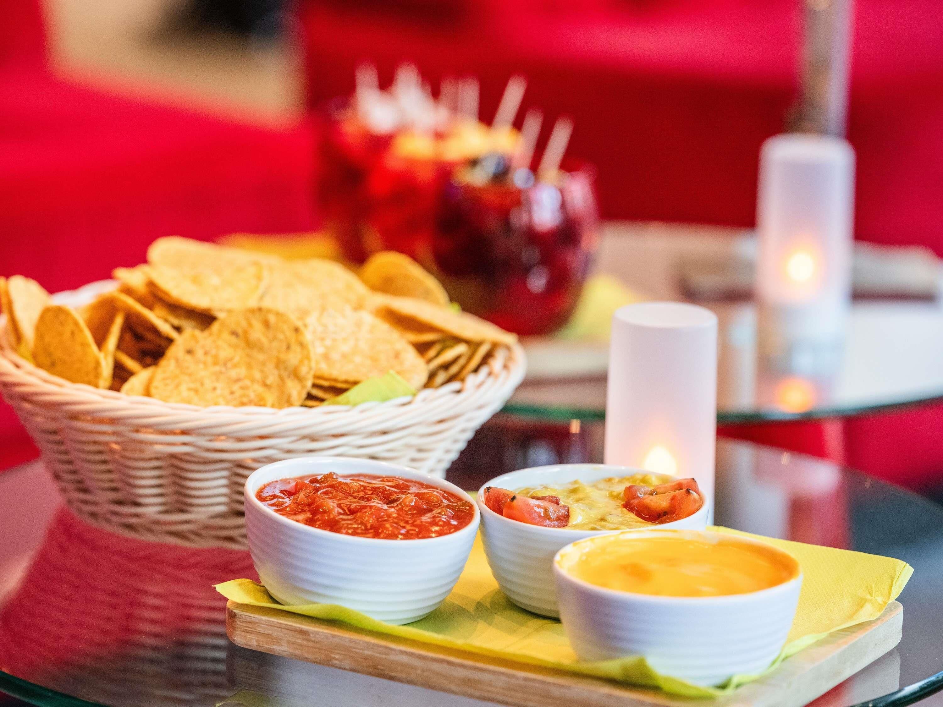 Una mesa con una cesta de papas fritas, dos recipientes de salsas y una vela.