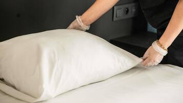Una persona acomodando un almohadón blanco sobre una cama.