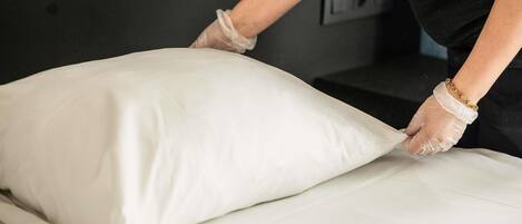 Una persona acomodando un almohadón blanco sobre una cama.