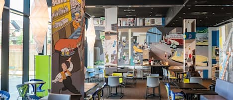 Un interior de restaurante moderno con techos altos, murales coloridos y diversas opciones de asientos.