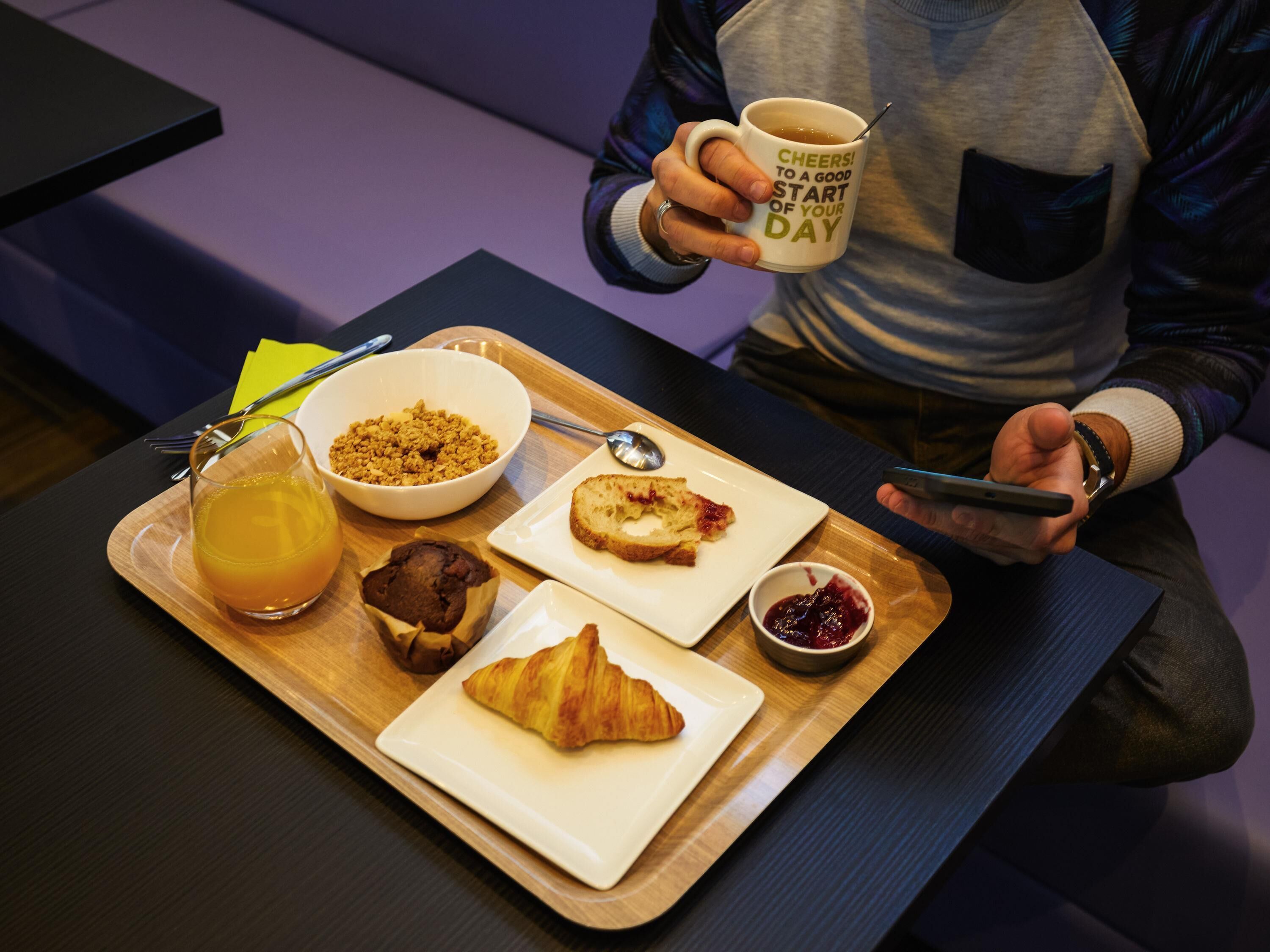 A tray with breakfast items including a croissant, muffin, and a bowl of cereal, along with a glass of orange juice and a cup of coffee.
