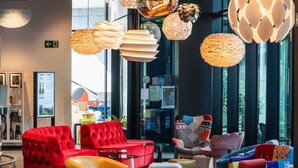 A modern interior with red and yellow seating, large windows, and various hanging light fixtures. - ibis Styles Liege Guillemins (Liege)