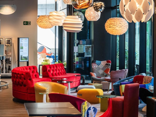 A modern interior with red and yellow seating, large windows, and various hanging light fixtures. - ibis Styles Liege Guillemins (Liege)