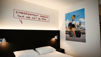 Une chambre d’hôtel avec un lit, un mur orné d’une illustration de style bande dessinée et un panneau avec du texte en français.