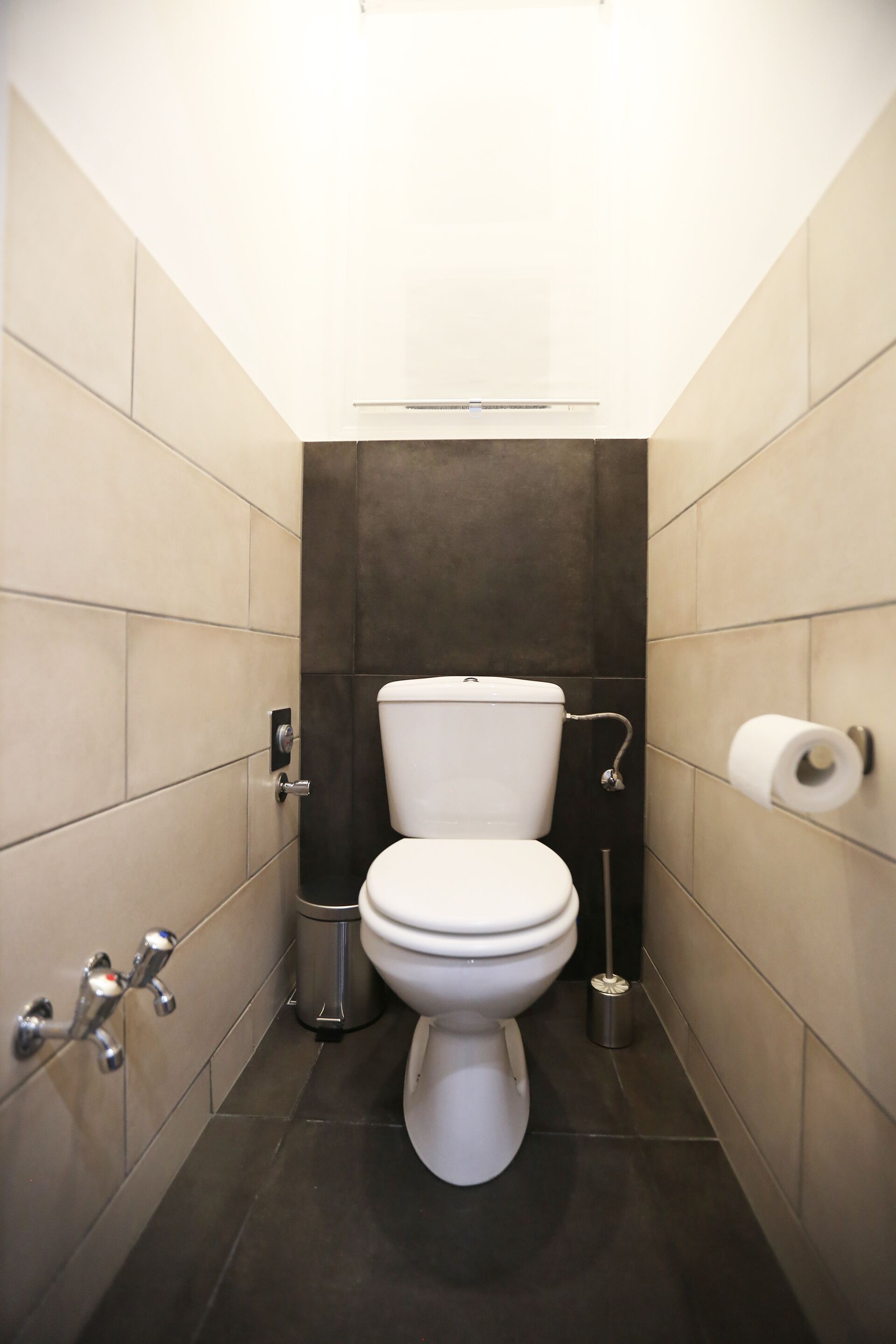 Un baño pequeño y moderno con inodoro, un bote de basura y un dispensador de papel higiénico.