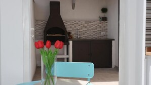 A dining area with a table and chair, a vase with red flowers, and a kitchen in the background. - iFicu (Catania)