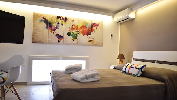 A modern hotel room with a large bed, a flat-screen TV mounted on the wall, and a large abstract painting above the bed. - iFicu (Catania)