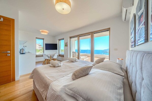 Ein Schlafzimmer mit einem großen Bett, einem Schreibtisch, einem Stuhl, einem Fernseher und Meerblick.