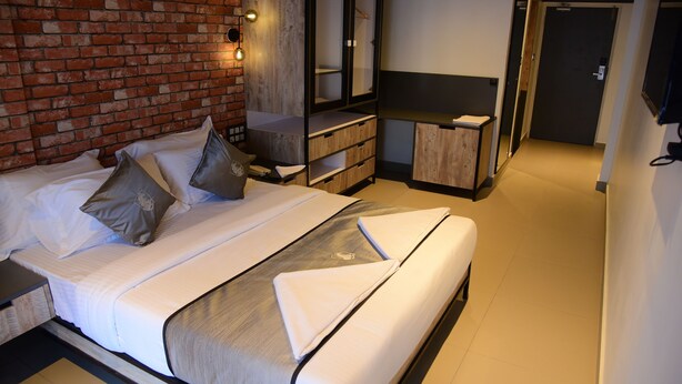 A modern hotel room with a brick wall, a large bed with white linens, a wooden dresser, and a television mounted on the wall. - VITS Select Kudro Destinn (Mangaluru)