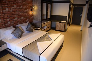 A modern hotel room with a brick wall, a large bed with white linens, a wooden dresser, and a television mounted on the wall. - VITS Select Kudro Destinn (Mangaluru)