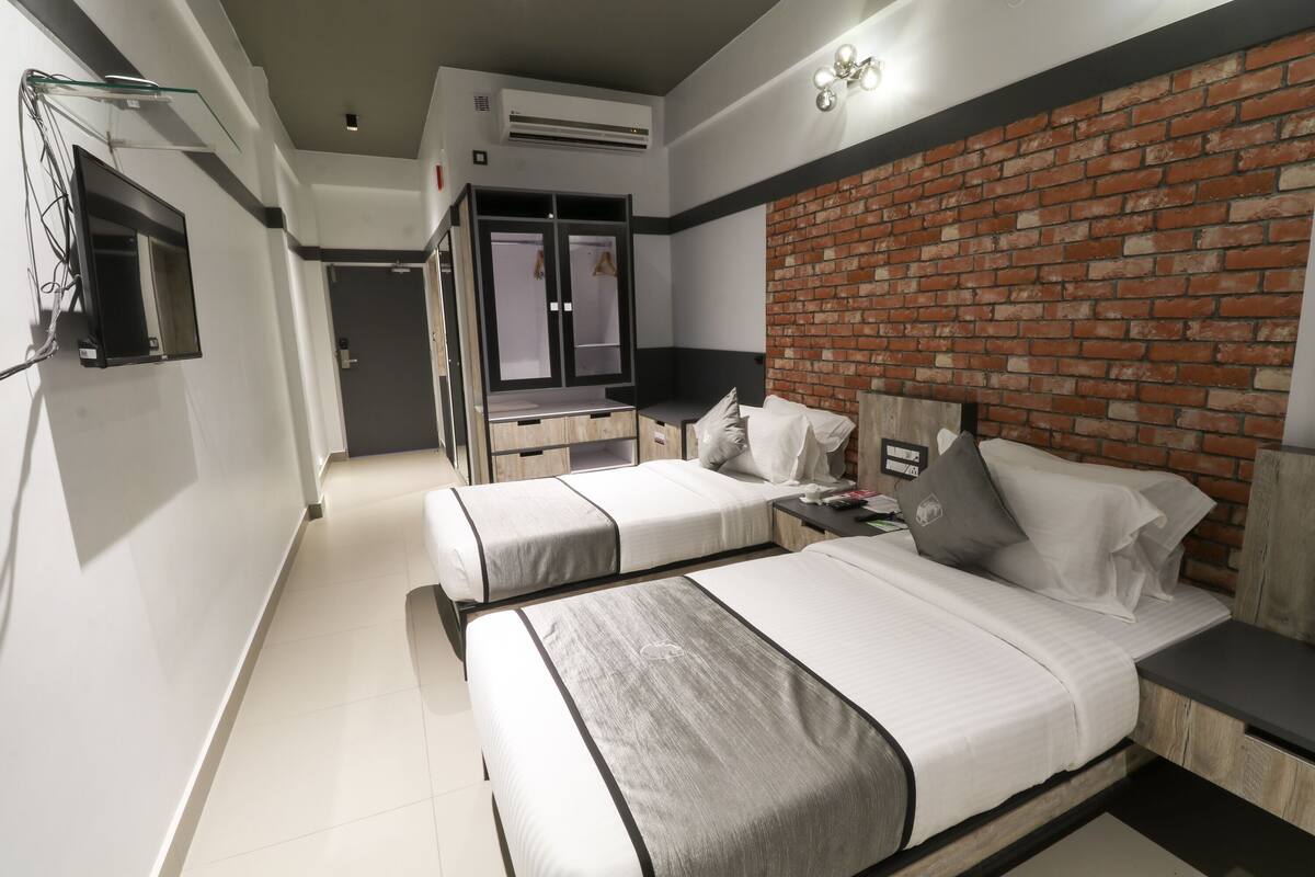 Et moderne hotelværelse med to senge, et skrivebord og en væg med murstensudsmykning.