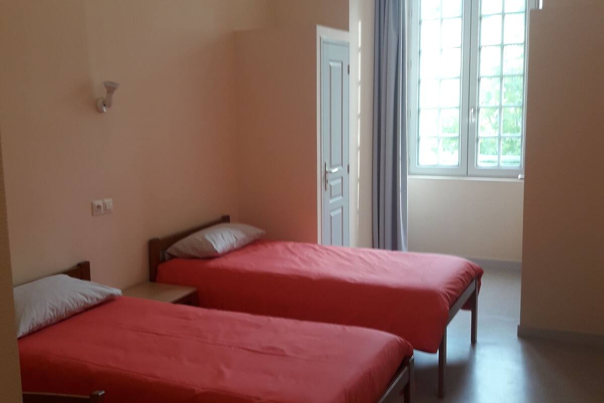 A room with two beds, a small table, and a window with curtains.