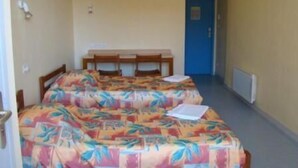 A room with two beds, a desk, and a blue door. - Hostellerie Charles de Foucauld (Viviers)
