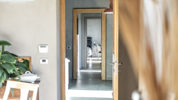 A hallway leading to a bedroom with a bed, bedside table, and lamp. There is a plant on the left and a door frame on the right. - Agriturismo Villa Gelso (Vesime)