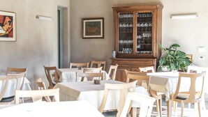 A dining area with wooden tables and chairs, a wooden cabinet with glass doors, and a potted plant. - Agriturismo Villa Gelso (Vesime)