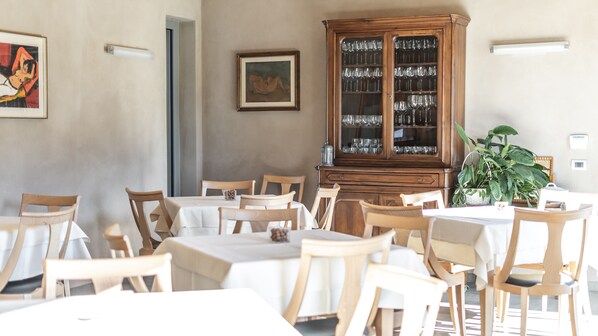 A dining area with wooden tables and chairs, a wooden cabinet with glass doors, and a potted plant.