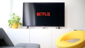 A modern living room with a flat-screen TV displaying the Netflix logo, a potted plant, and a yellow chair. - Paulay Central Top Studio (Budapest)