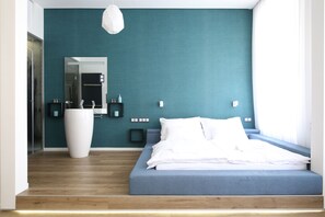 A modern bedroom with a large bed, a white vase, and a teal accent wall. - Paulay Central Top Studio (Budapest)
