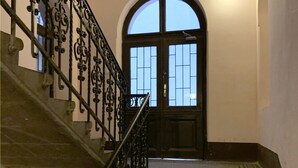 A staircase with ornate black metal railings leading to a door with a glass panel. - Paulay Central Top Studio (Budapest)