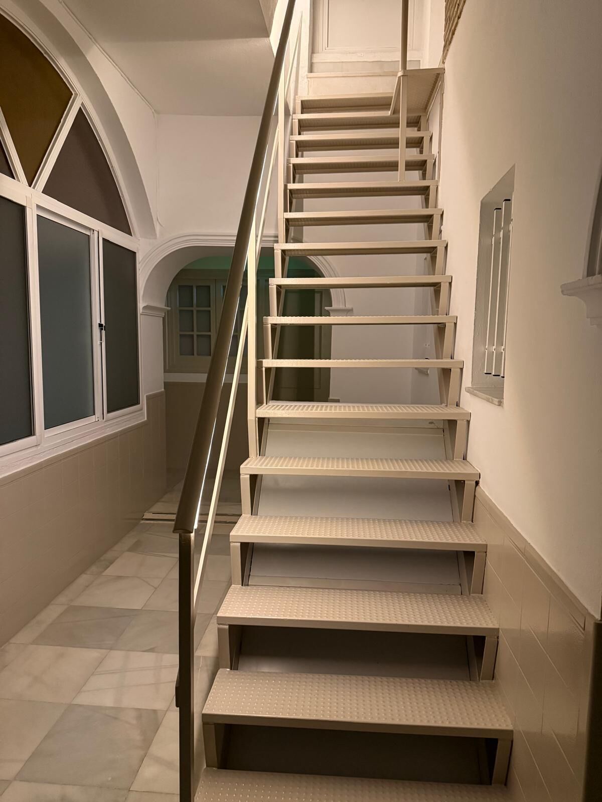 A staircase with a handrail, leading to a landing with a window.