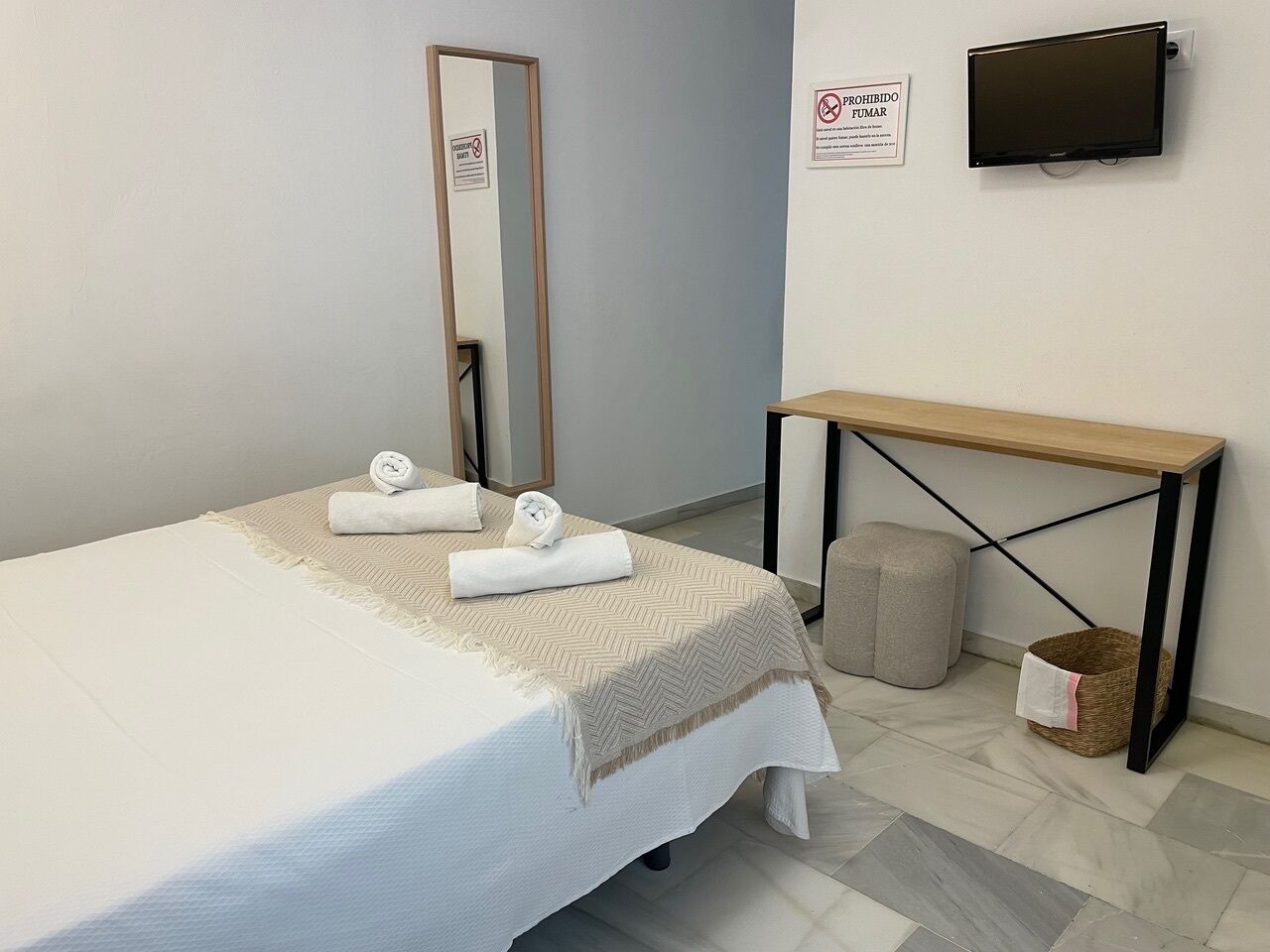 Una habitación de hotel con una cama, un espejo, un televisor, una mesa de madera y un banco.