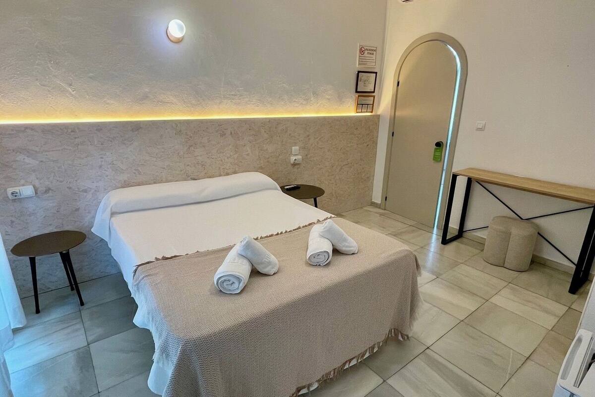 Een hotelkamer met een bed, twee nachtkastjes, een bankje en een douchegedeelte.